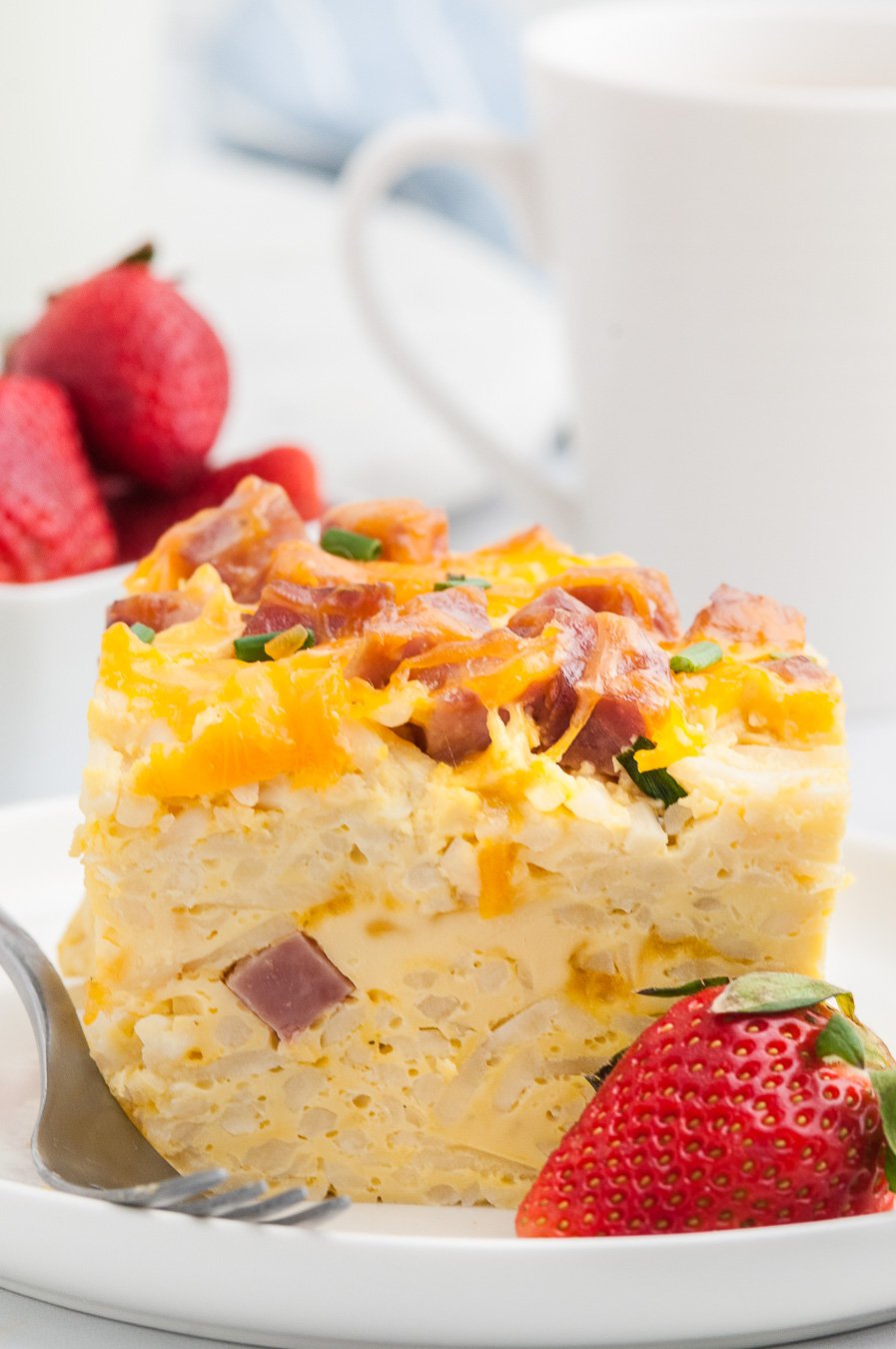 up close view of tall egg breakfast casserole. Fresh strawberry garnish.