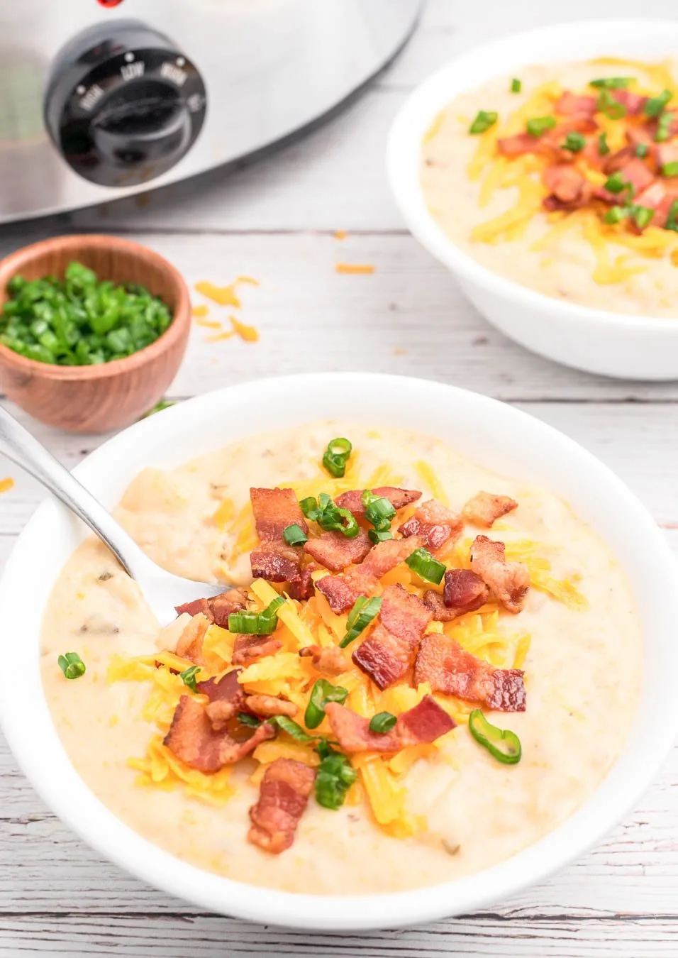 loaded baked potato soup served in a bowl with slow cooker and green onion garish in the background