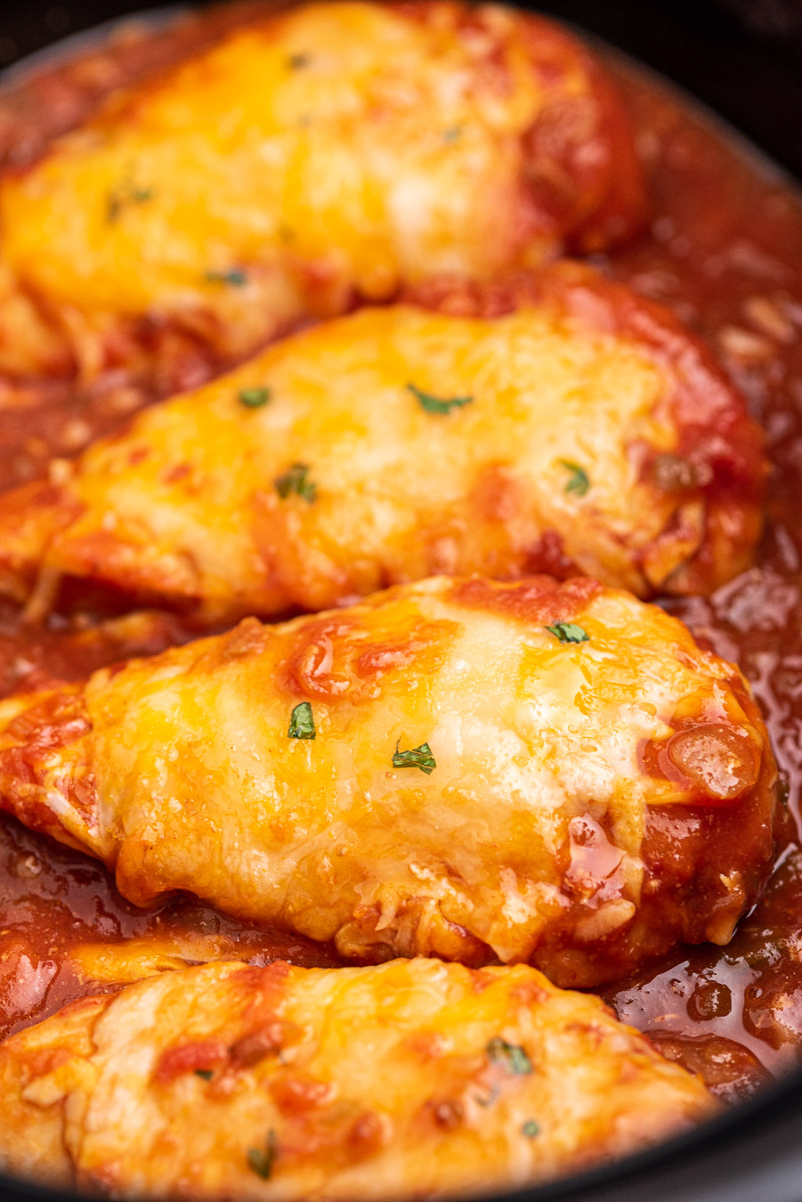 up close view of prepared chicken breasts in a slow cooker topped with cheese and cilantro