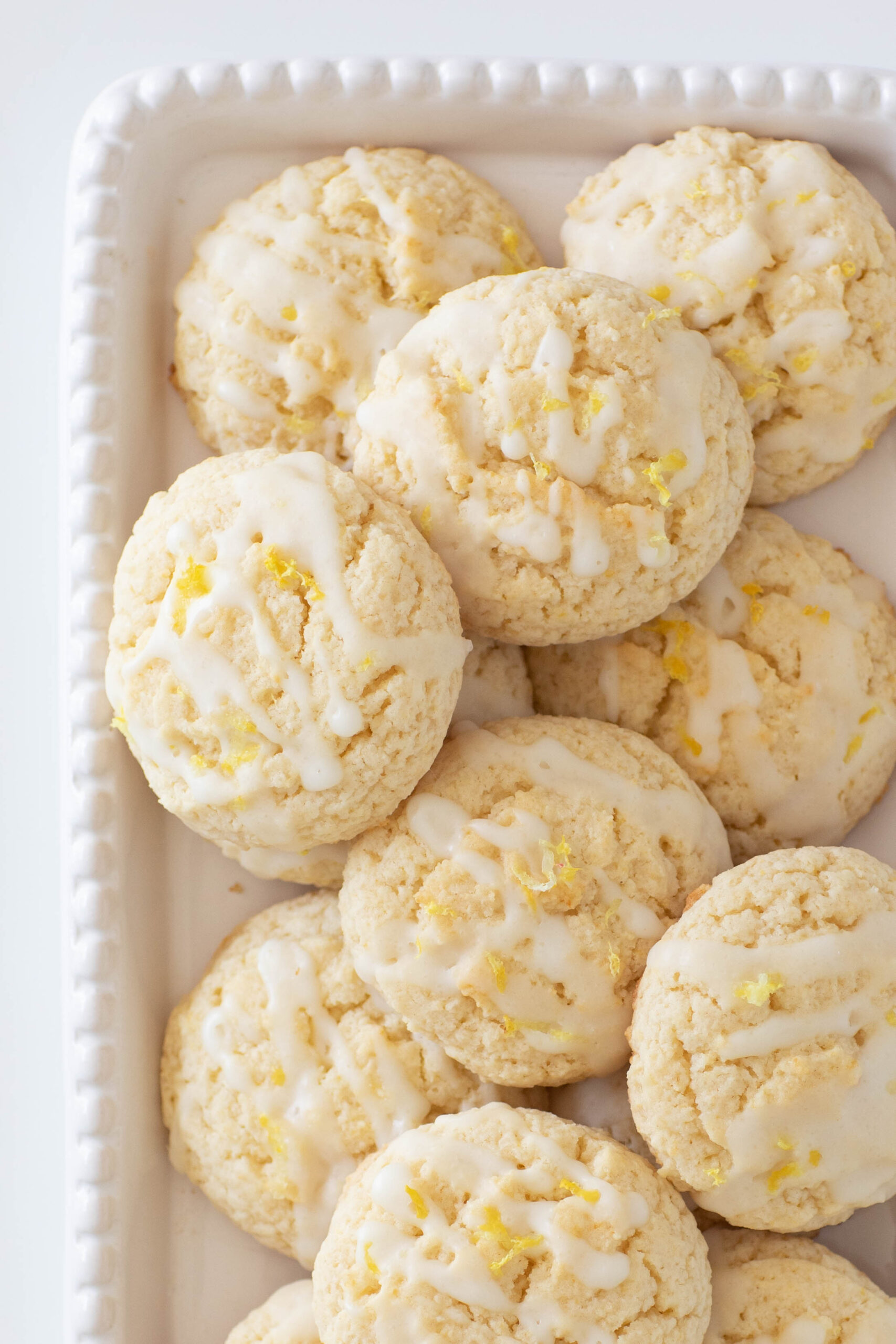 half plate of lemon cookies with white drizzle and lemon zest on top.