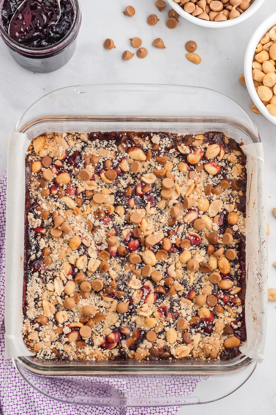 over the top view of a baking dish with baked dessert bars inside covered with chopped nuts, jelly and
