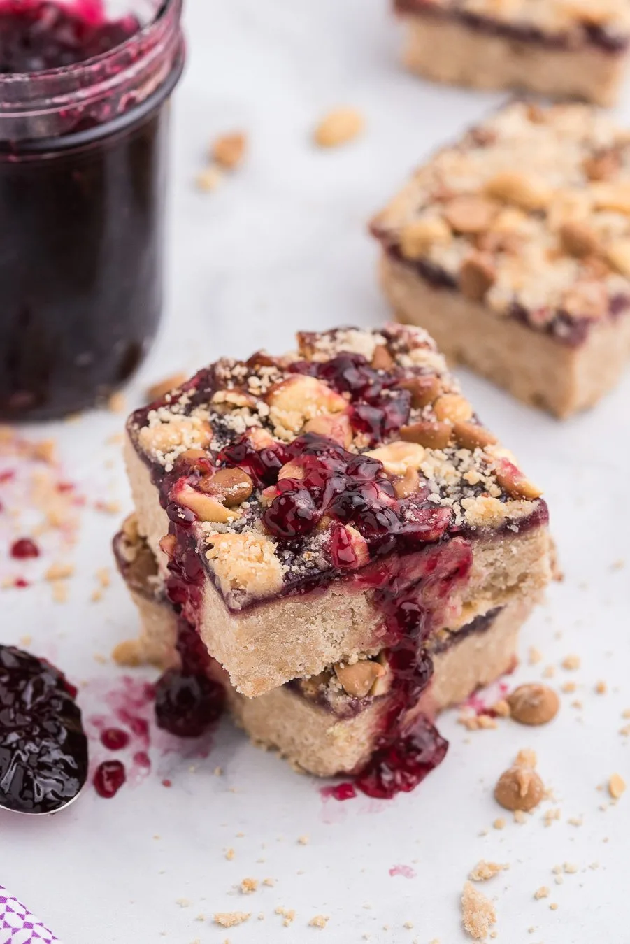 peanut butter and jelly bars with oozing jelly, chopped peanuts and peanut butter chips. jar of jelly in background