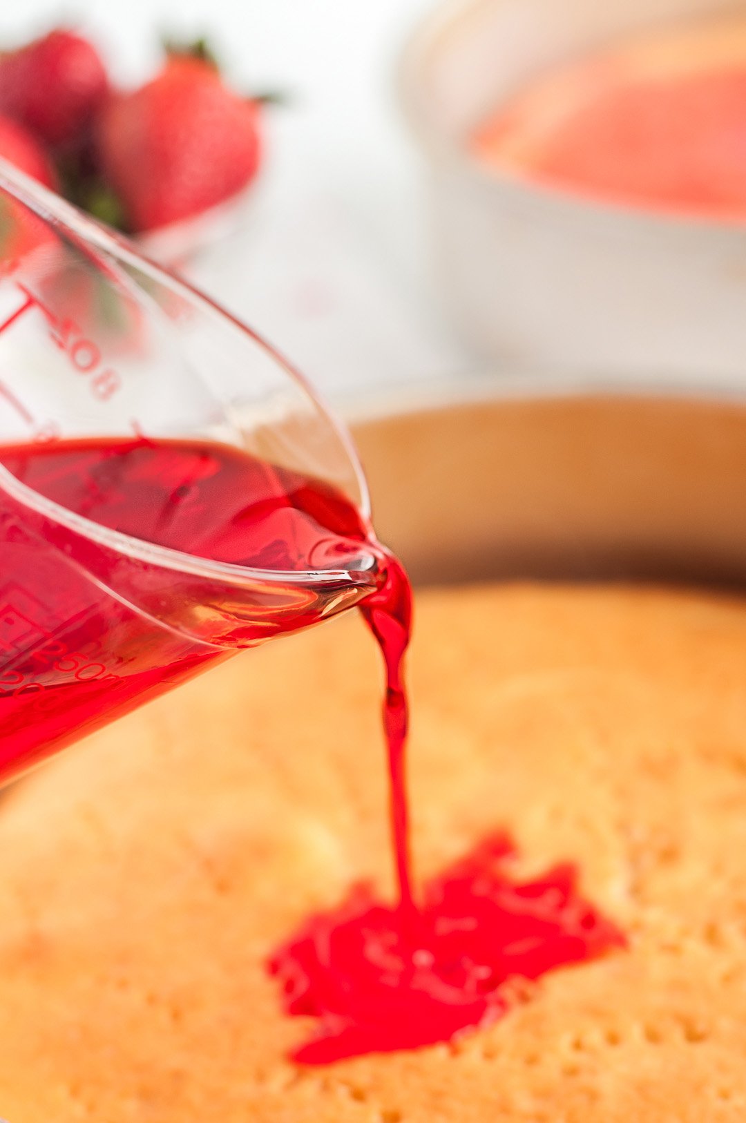 pouring jello onto baked cake to make poke cake