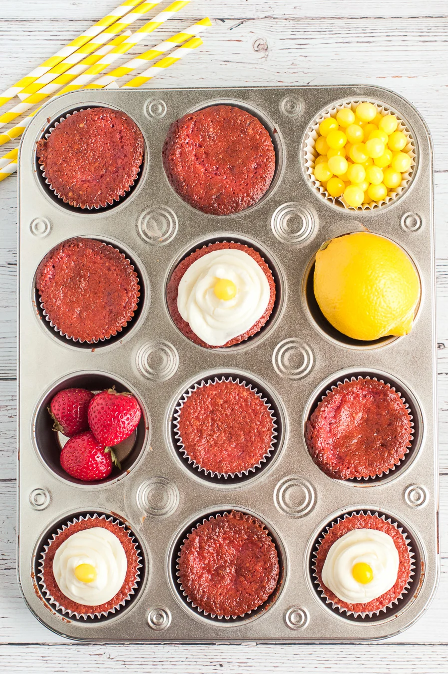 muffin tin with cupcake ingredients inside of it. strawberries, frosting and more