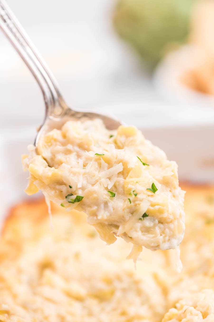 up close spoonfull of baked cheesy artichoke dip