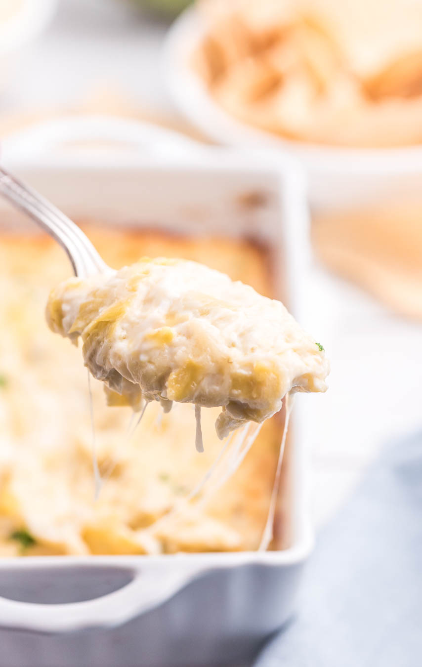 spoon full of artichoke dip being scooped out of baking dish