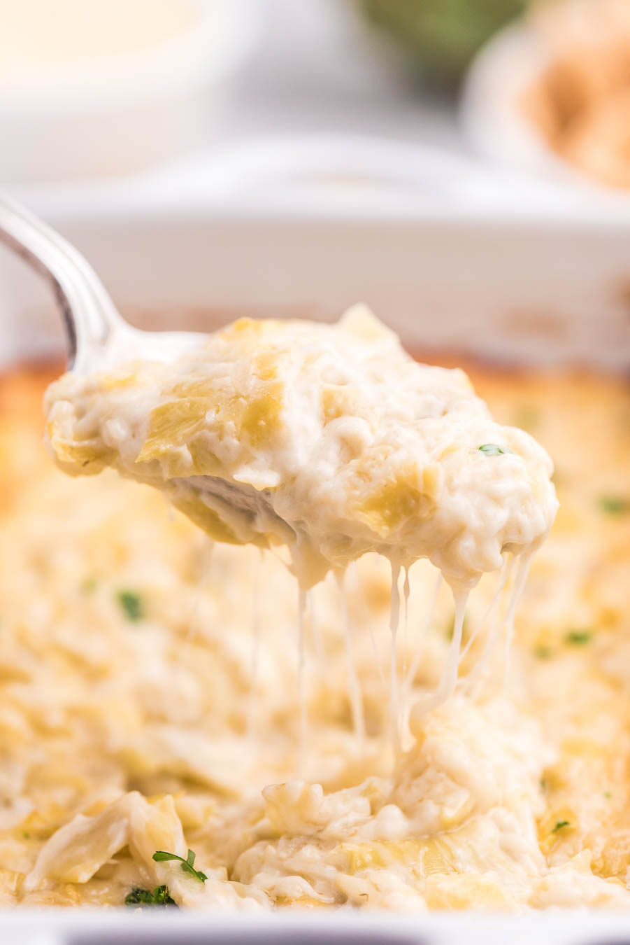spoonful of melty cheesy artichoke dip from the baking dish