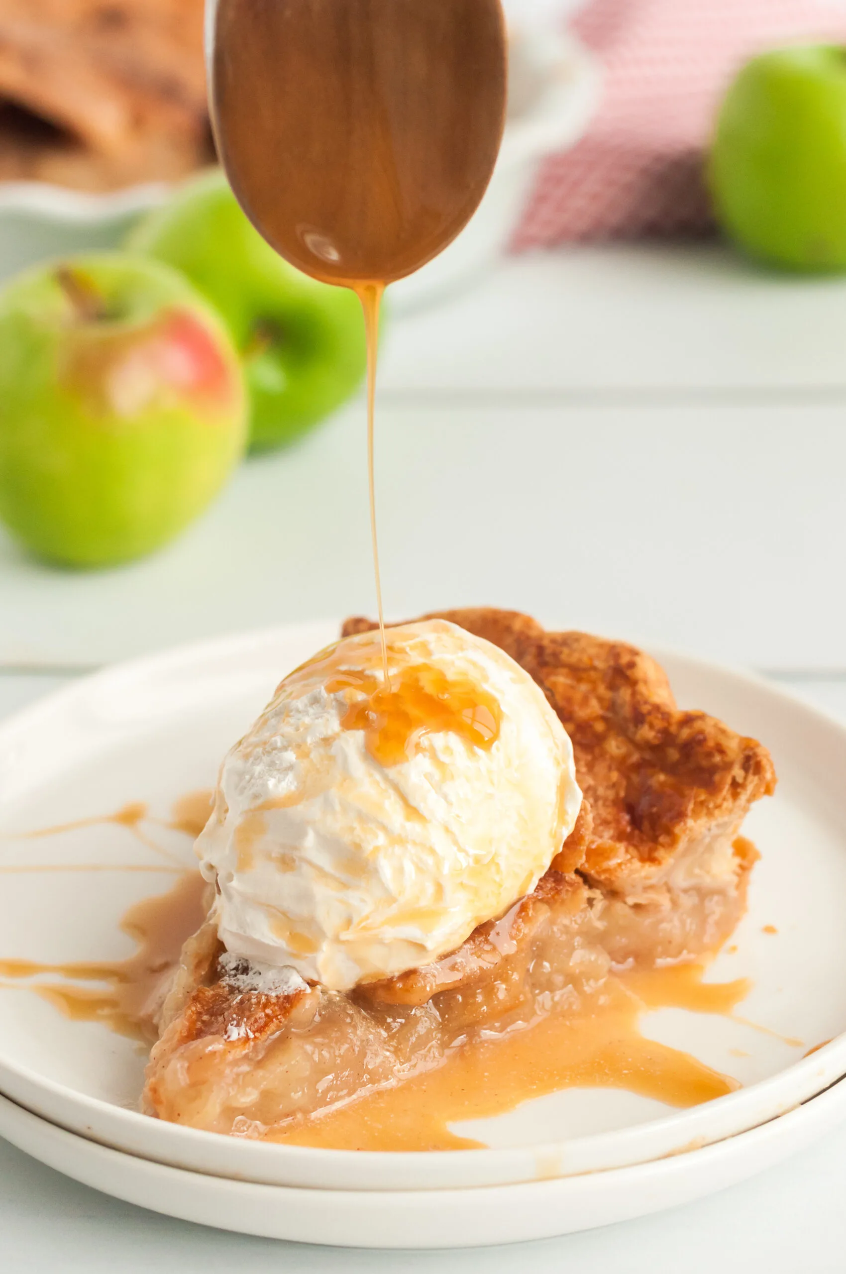 apple pie slice on a plate with caramel being drizzled on top
