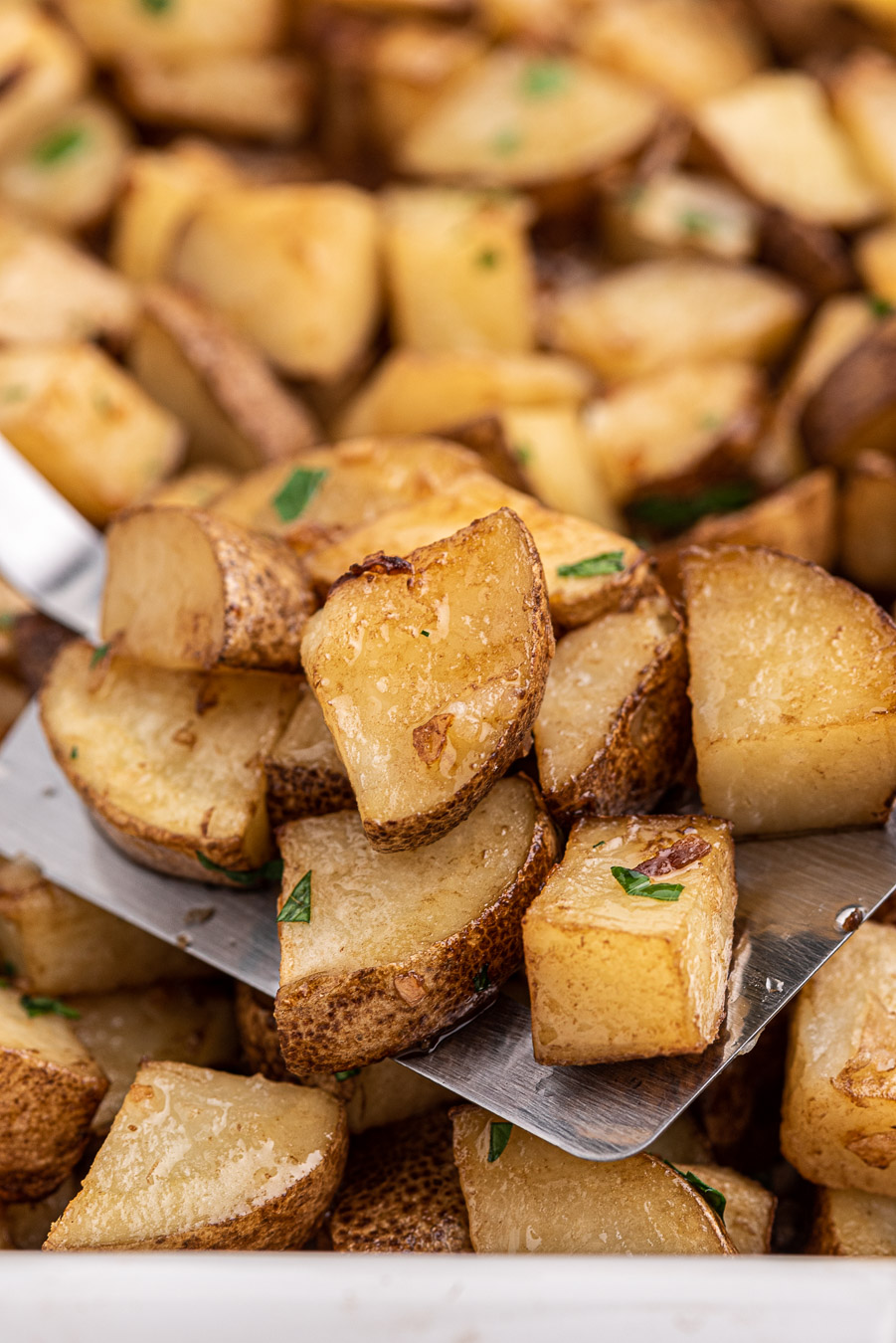 Easy roasted potatoes. spatula scooping roasted potatoes up out of a big dish of them