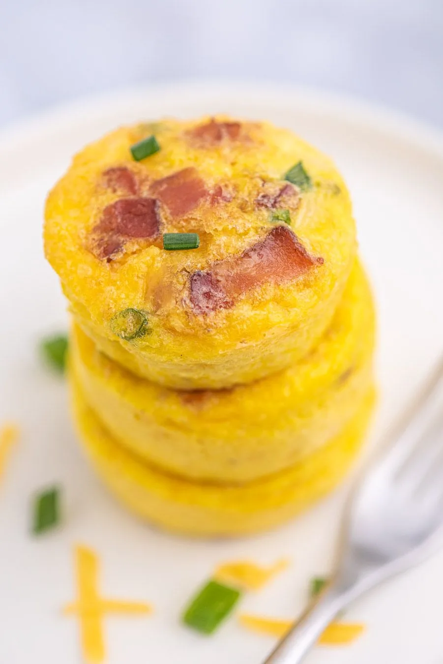 up close view of a stack of egg omelet cups that were made in a muffin tin. Bacon and chives as garnish.
