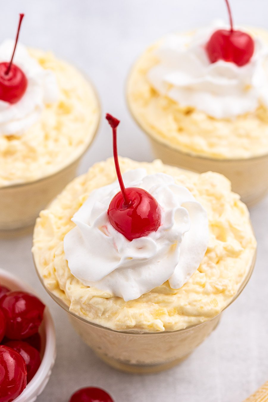 angled down view of pineapple pudding served in individual dishes with whipped cream and a cherry on top
