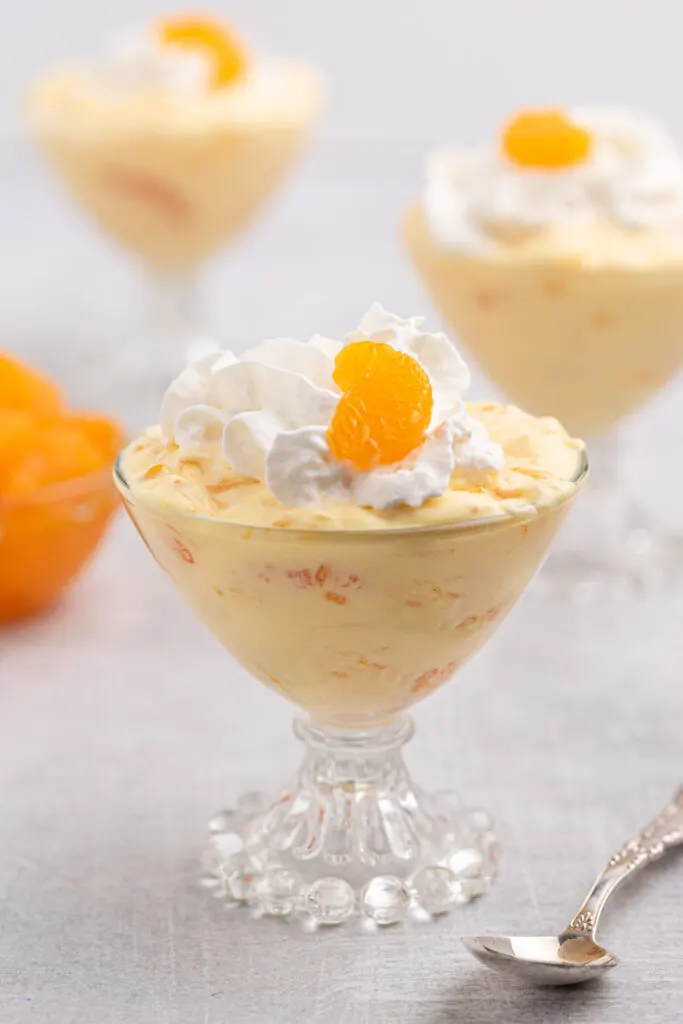 mandarin dessert made with 3 ingredients, served in a vintage glass dish and topped with whipped cream and a mandarin orange slice