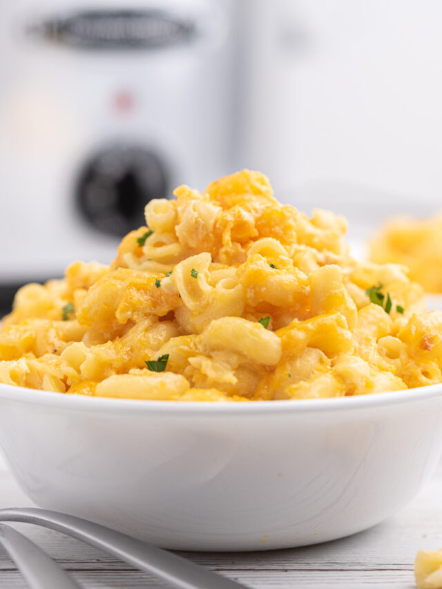 tall bowl of mac and cheese. slow cooker pictured in background