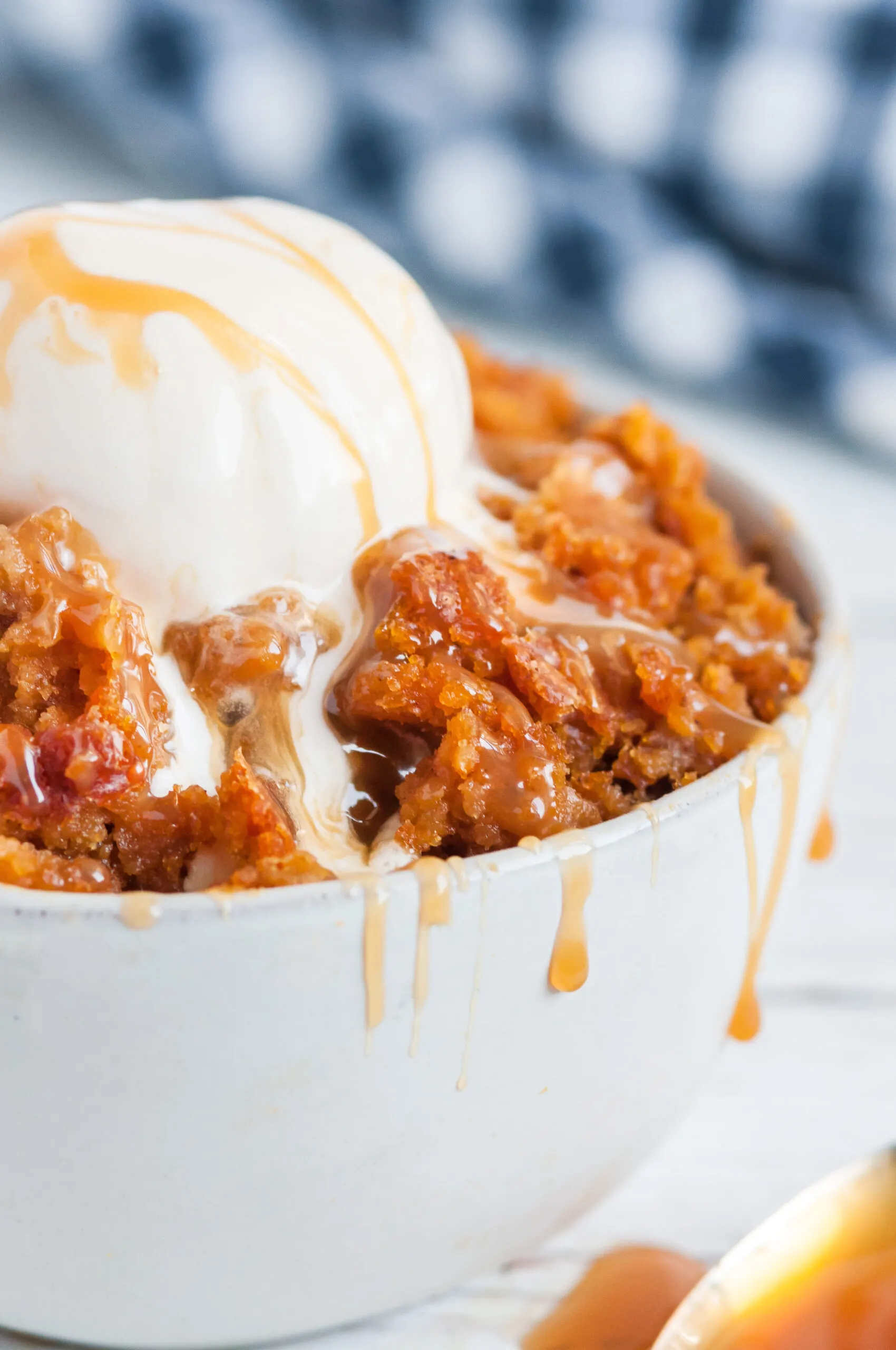 pumpkin dump cake in a bowl with oozy caramel and melting ice cream scoop