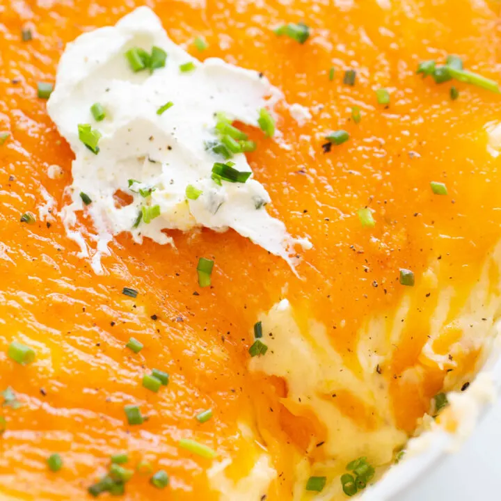 cheddar mashed potatoes baked in a dish up close. garnished with chopped chives, sour cream and black pepper