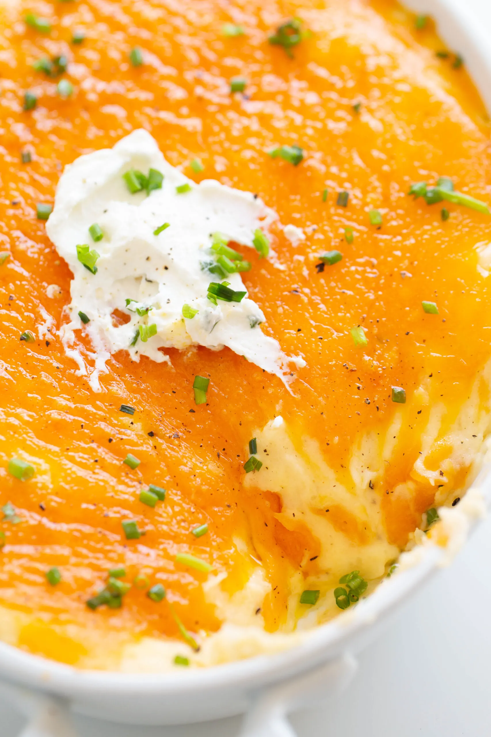 cheddar mashed potatoes baked in a dish up close. garnished with chopped chives, sour cream and black pepper