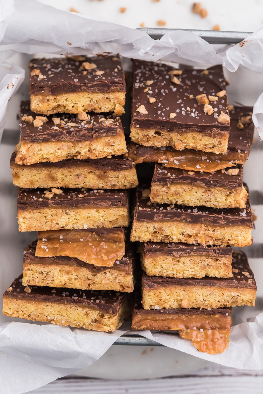 salted caramel bars with chocolate on top stacked into a container lined with parchment paper