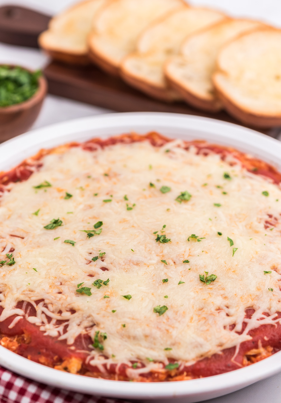 chicken parmesan dip in a dish covered with cheese and green hebs