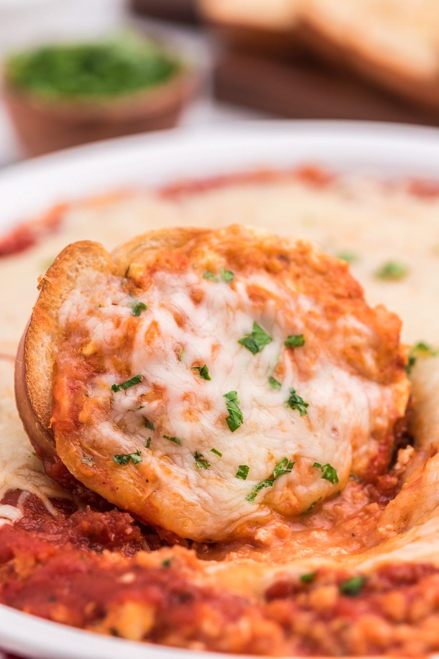 small piece of fresh bread slathered with cheese, sauce and a dash of green herbs