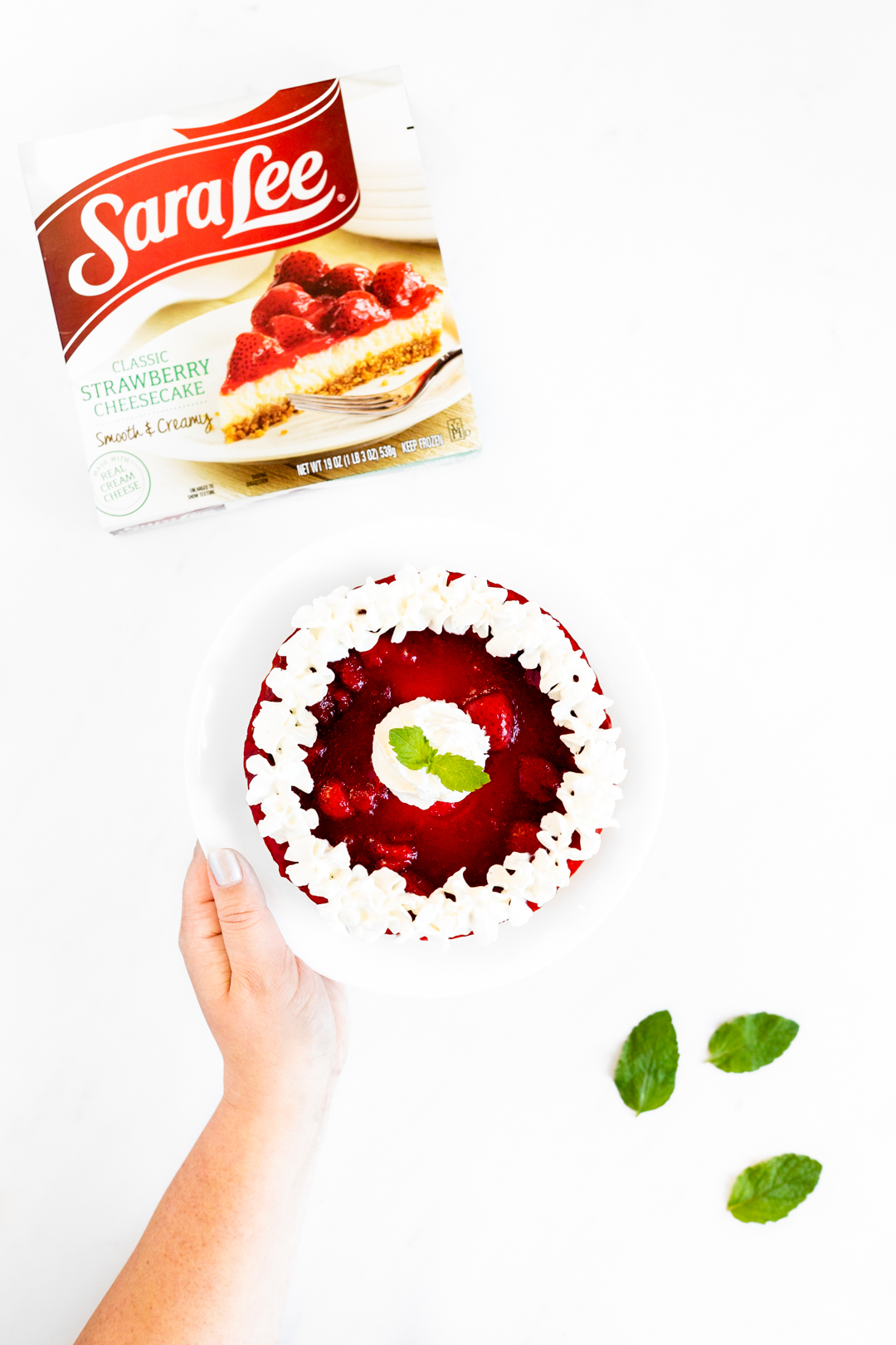 Strawberries and cream cheesecake being held with mint.