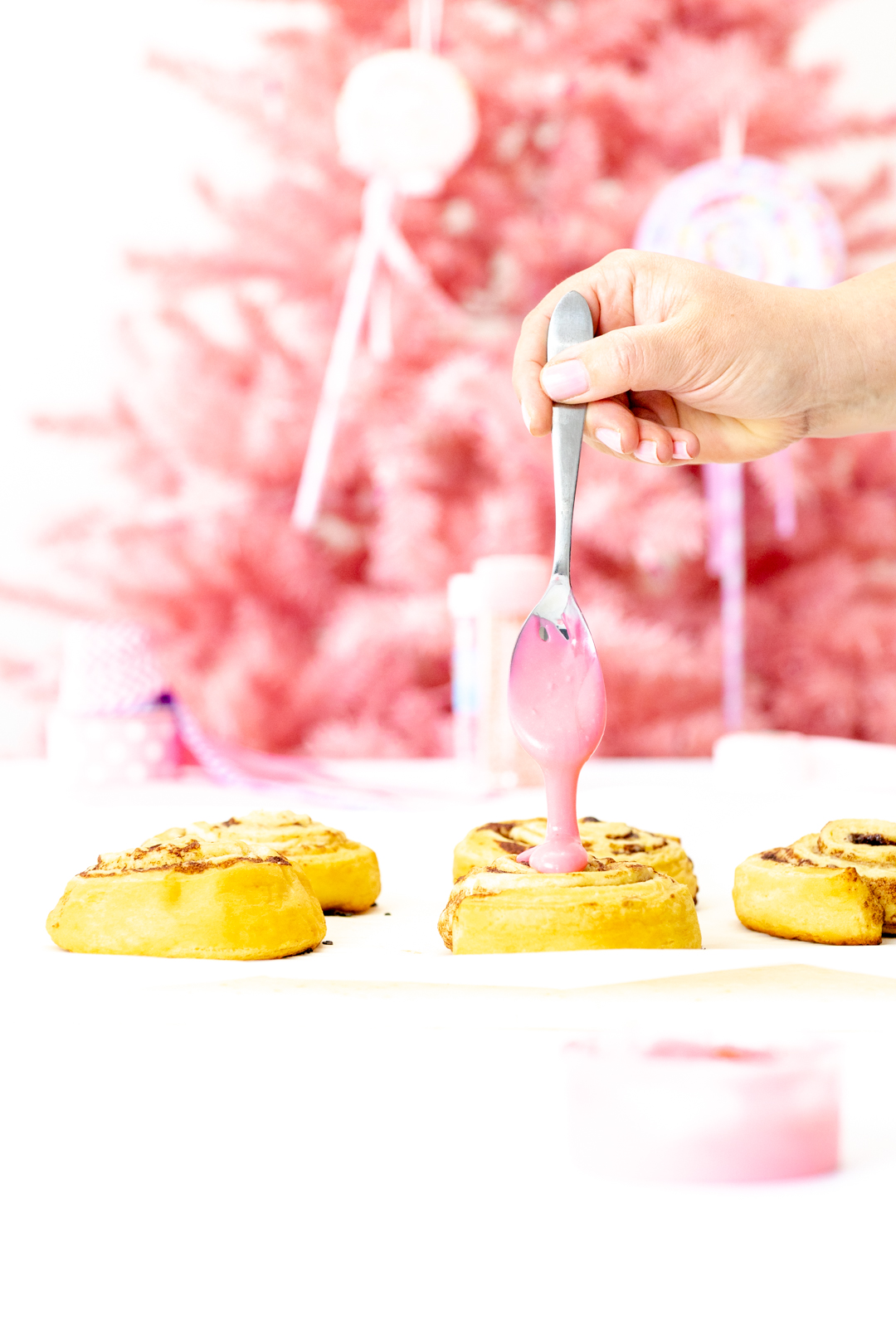 drizzling pink icing on cinnamon rolls