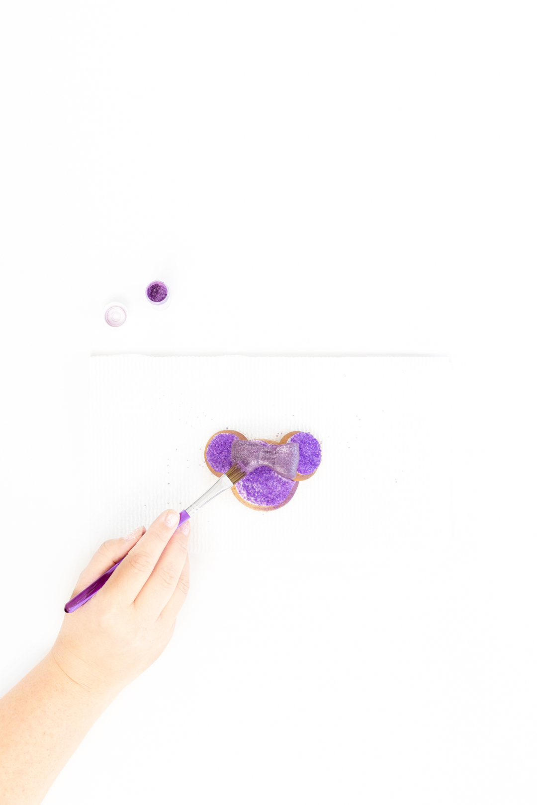 painting glitter dust onto purple minnie mouse cookies