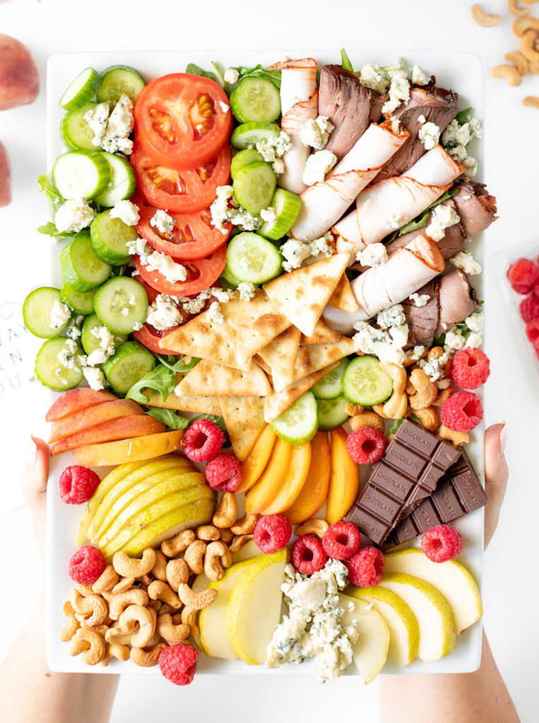 charcuterie board with mini cucumbers, turkey and roast beef, tomatoes, pitas.