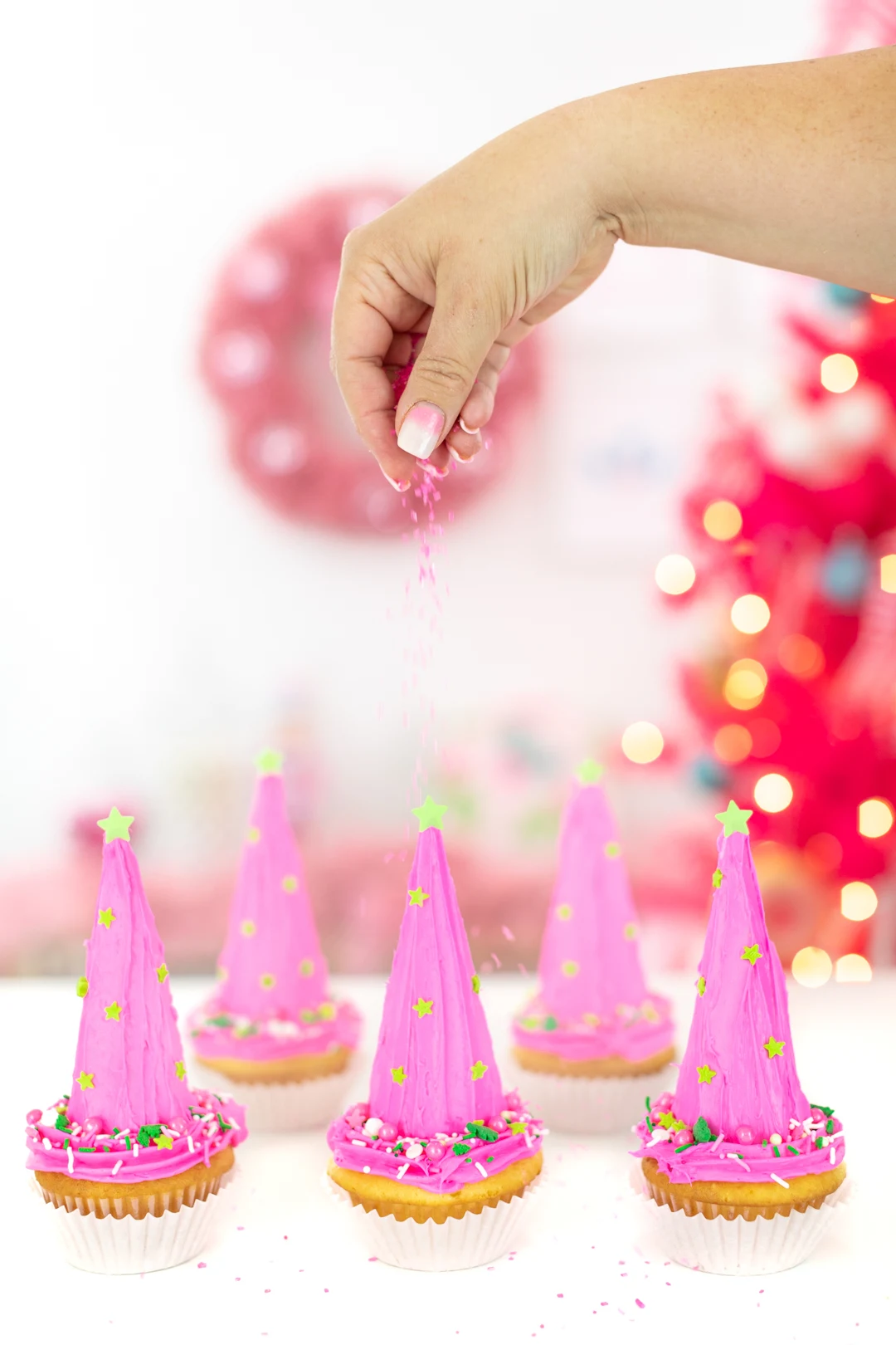 sprinkling pink sugar crystals over pink christmas tree cupcakes