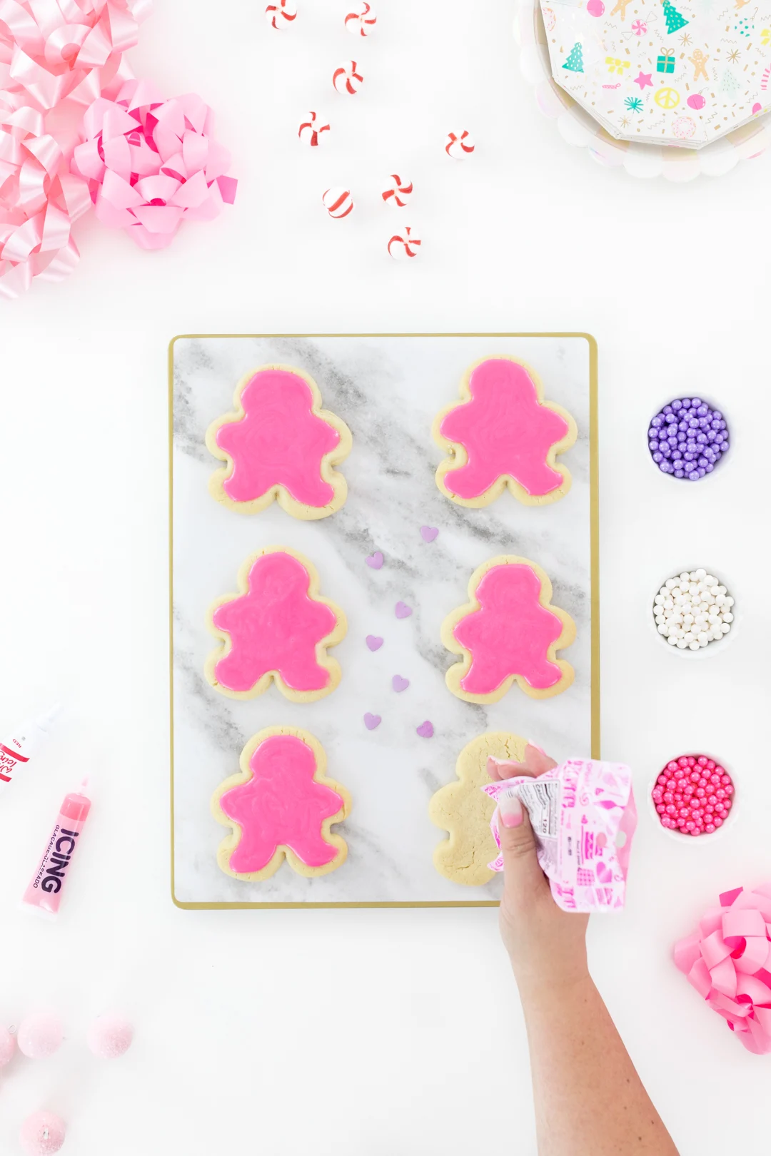 adding pink icing to gingerbread shaped sugar cookies