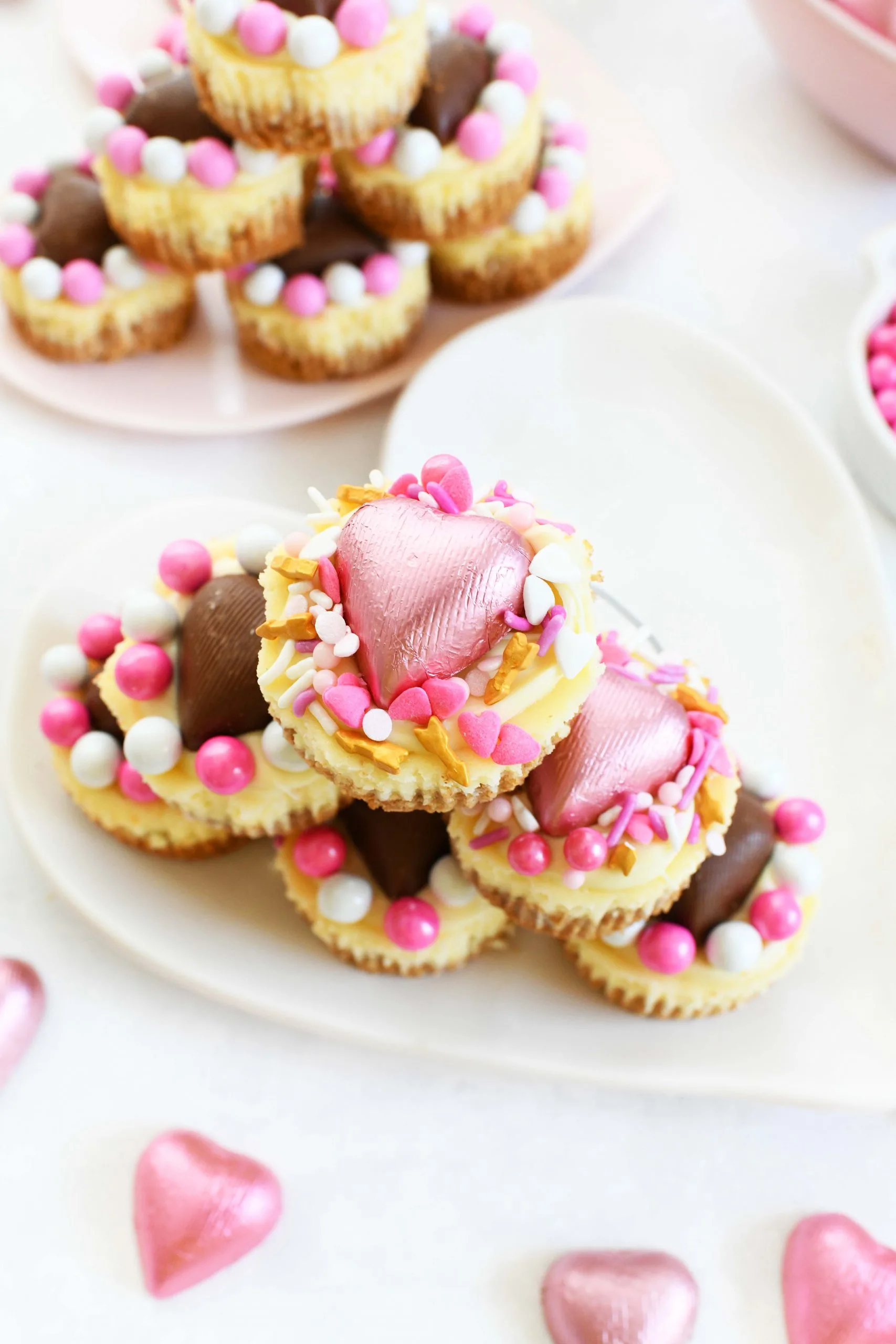 mini cheesecakes with valentine's day sprinkles and heart shaped chocolates on top.