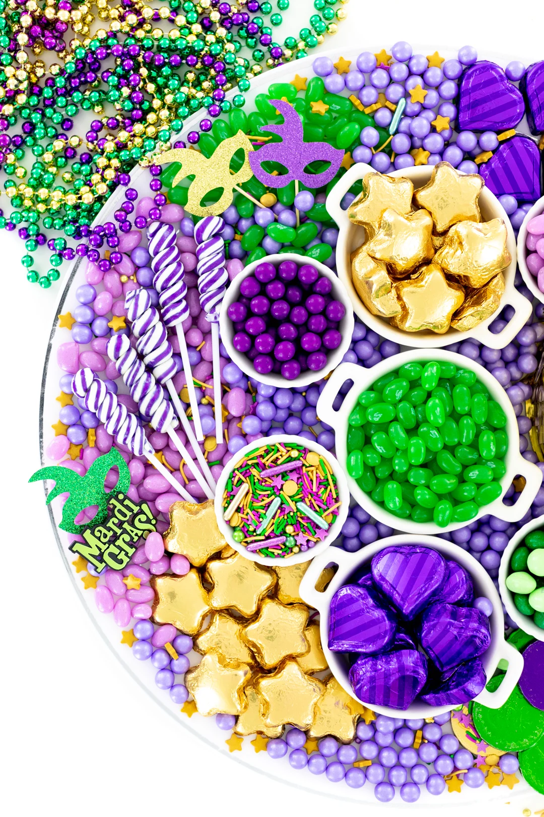 mardi gras candy grazing board with purple swirl lollipops and more green, purple and gold candies.