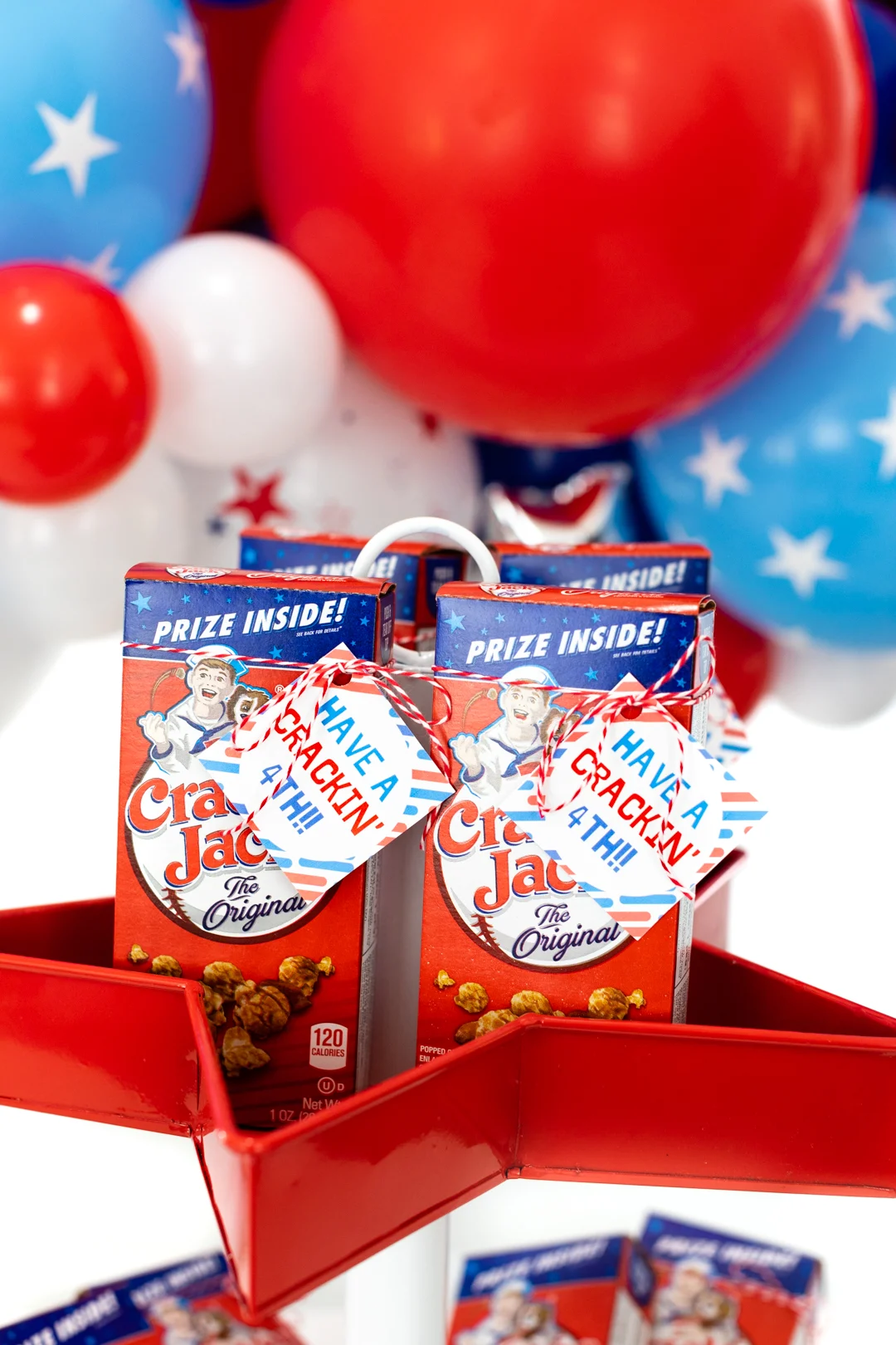 Individual boxes of cracker jack served on a 4th of july tray for parties. balloons in background