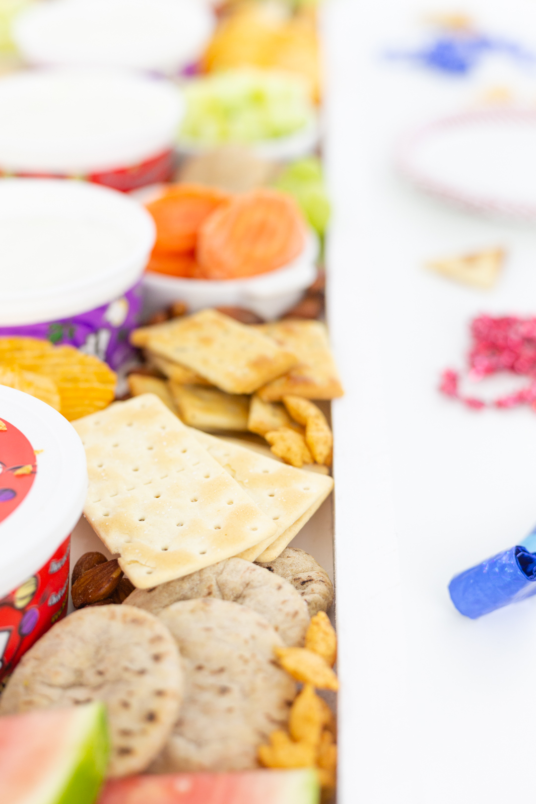 long rectangular charcuterie board with crackers, vegetables and dips