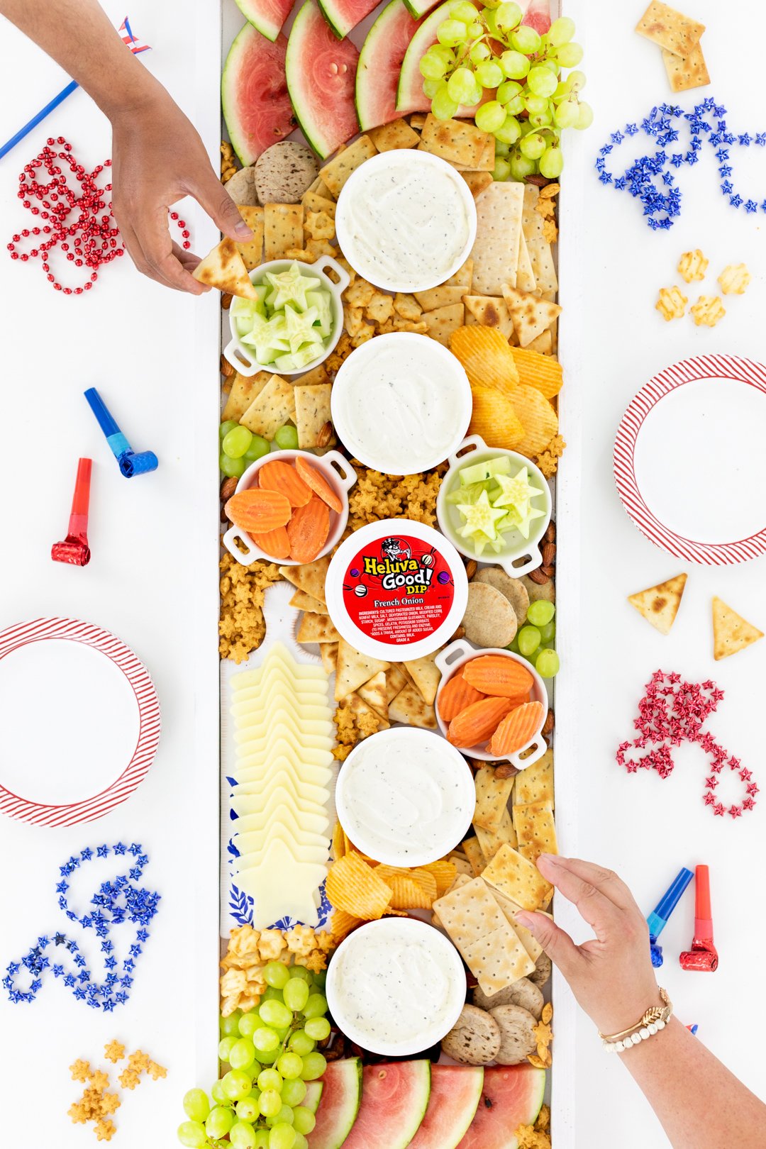 Hands grabbing snacks off of a huge charcuterie board.