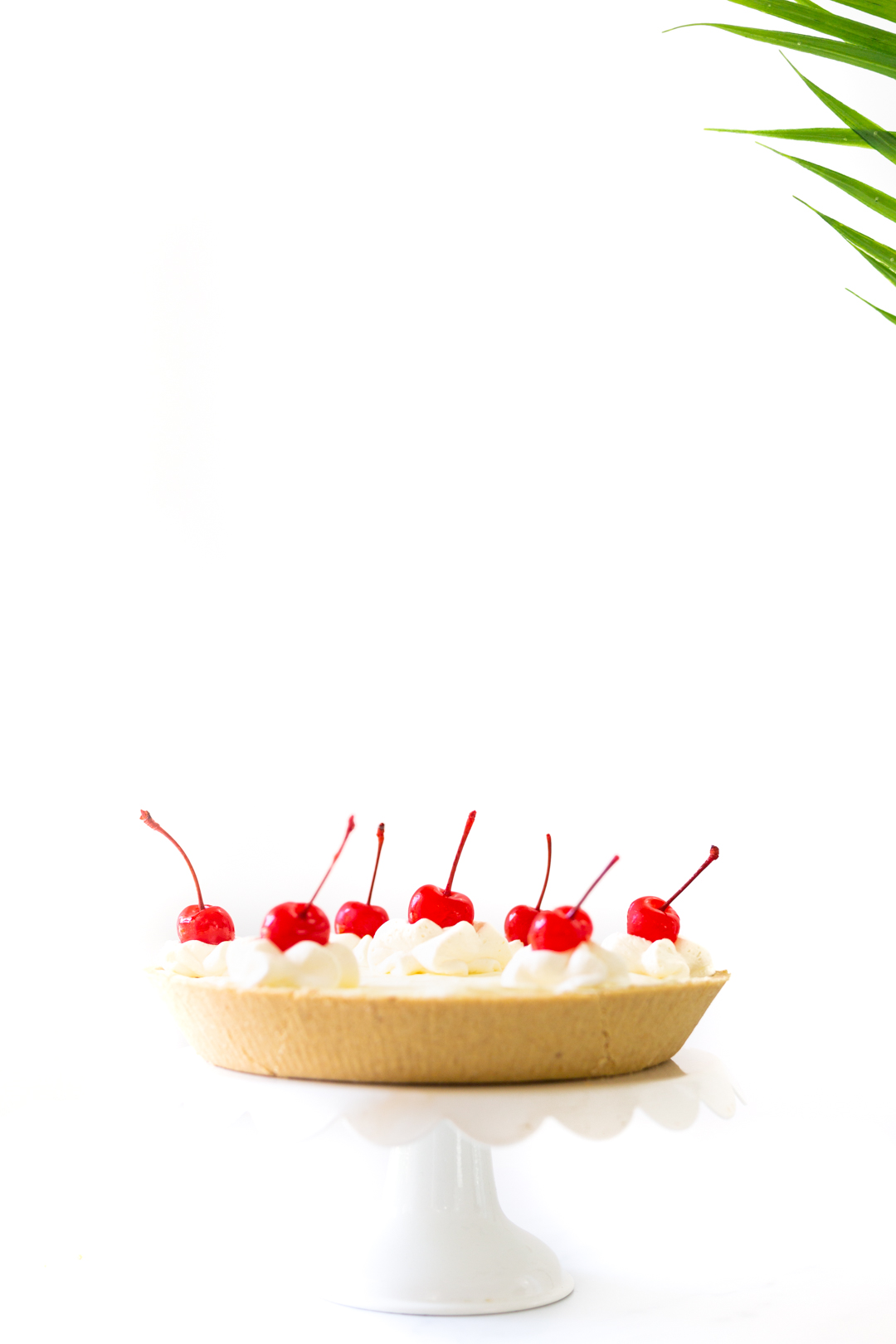 cake on a pedestal made with pineapple jello and topped with whipped topping and cherries