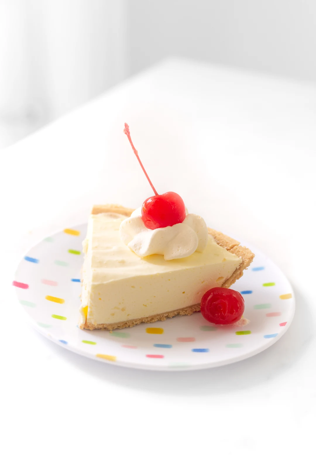 a slice of pineapple pie on a small plate and topped with a large stemmed cherry