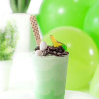 dino ice cream cup topped with crushed oreo cookie, candy eggs and gummy candy with a cute polka dotted wooden spoon.