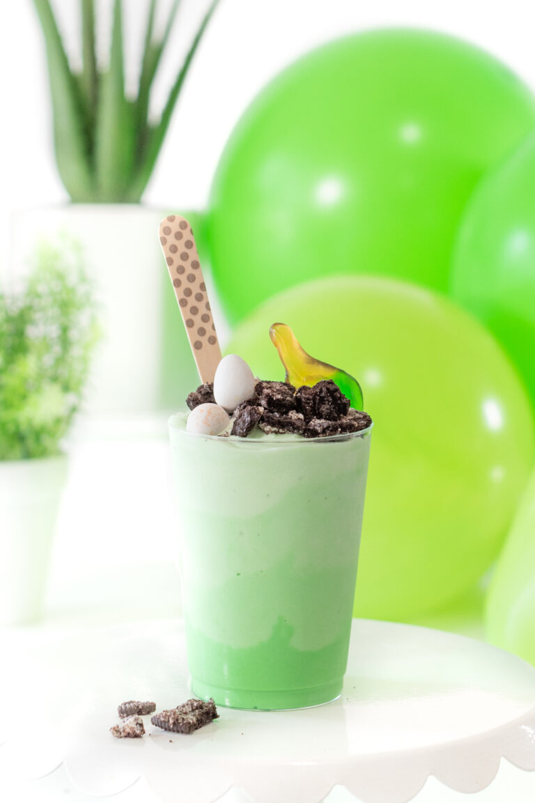 dino ice cream cup topped with crushed oreo cookie, candy eggs and gummy candy with a cute polka dotted wooden spoon.