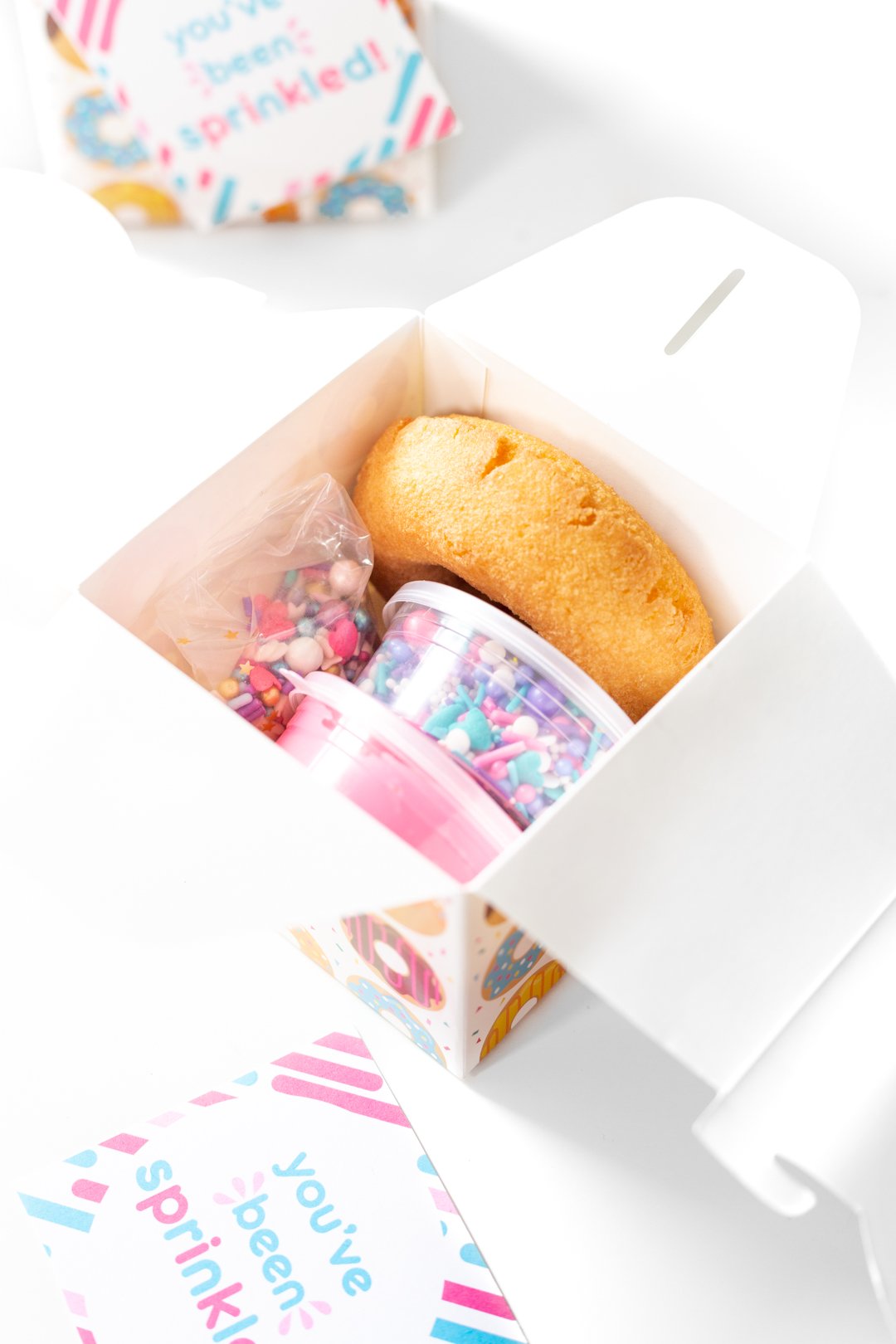 tiny donut decorating kit with containers of sprinkles and icing and a plain donut.