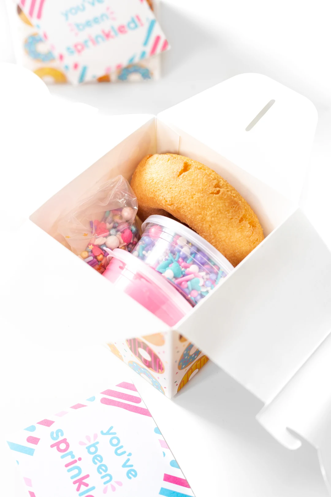 tiny donut decorating kit with containers of sprinkles and icing and a plain donut.