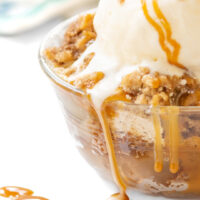 apple dump cake up close with apples and cake crumbs topped with ice cream and caramel