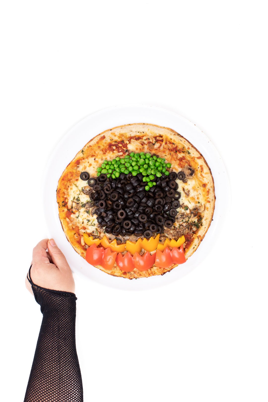 cooked pizza with a cauldron made of black olives with green pea ooze coming out of it. Red and and orange peppers for fire underneath.