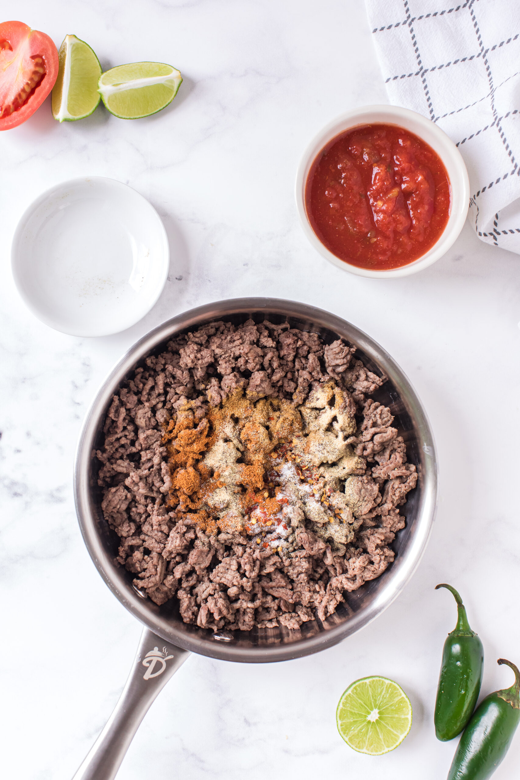 seasonings being added to a pan of cooked ground beef