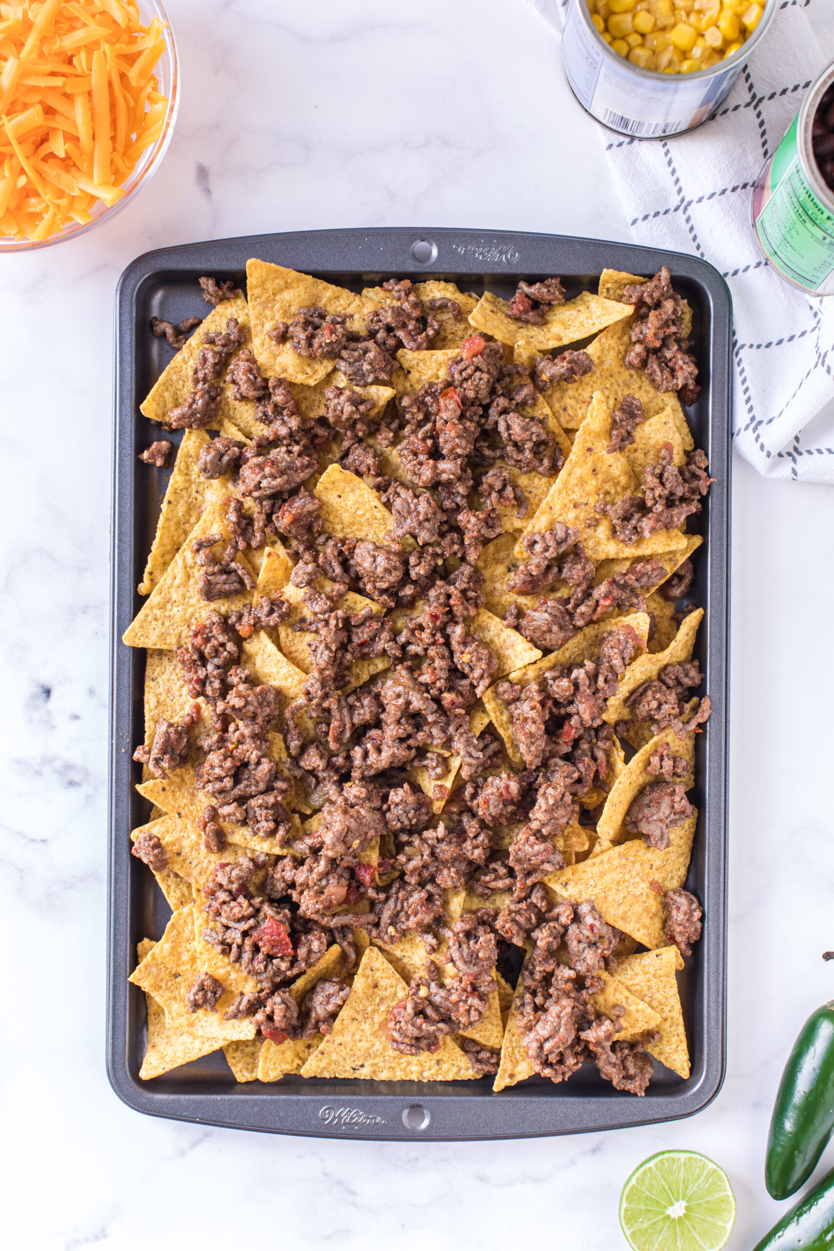 adding prepared beef to tray of nachos