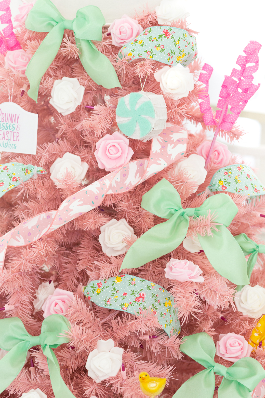 light pink christmas tree decorated for easter, up close view with decorations in focus. small flower heads, big mini ribbons, pink bunny ribbon used as garland.