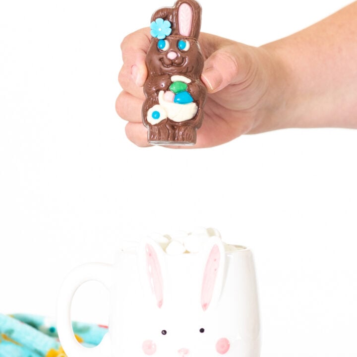 woman holding small chocolate easter bunny filled with hot cocoa mix above a mug.