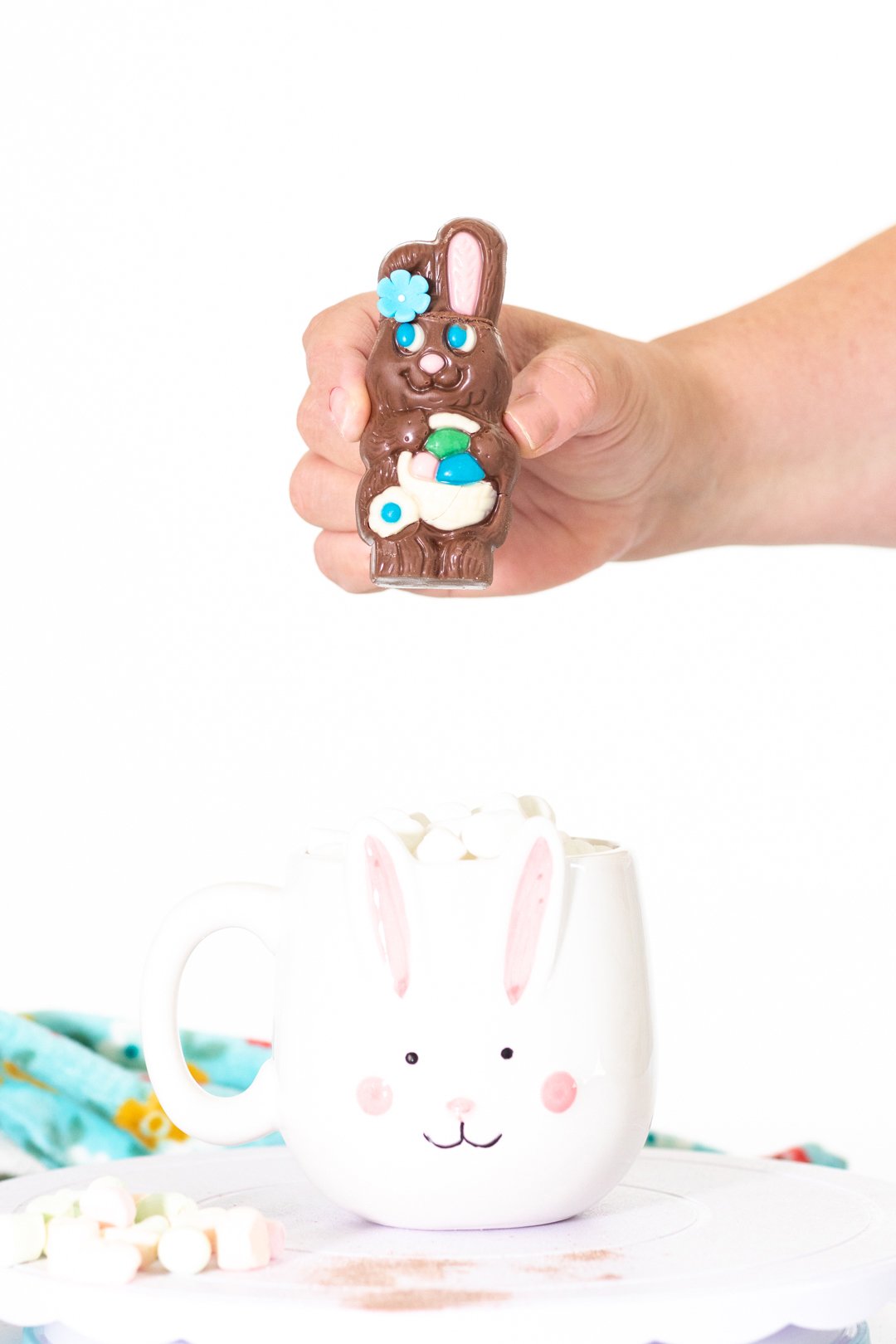 woman holding small chocolate easter bunny filled with hot cocoa mix above a mug.