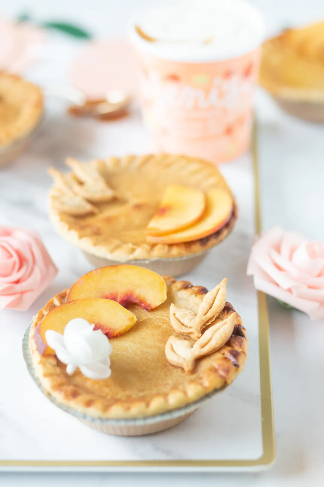 mini peach pie with peach slices, edible flower and pie crust leaves on top.