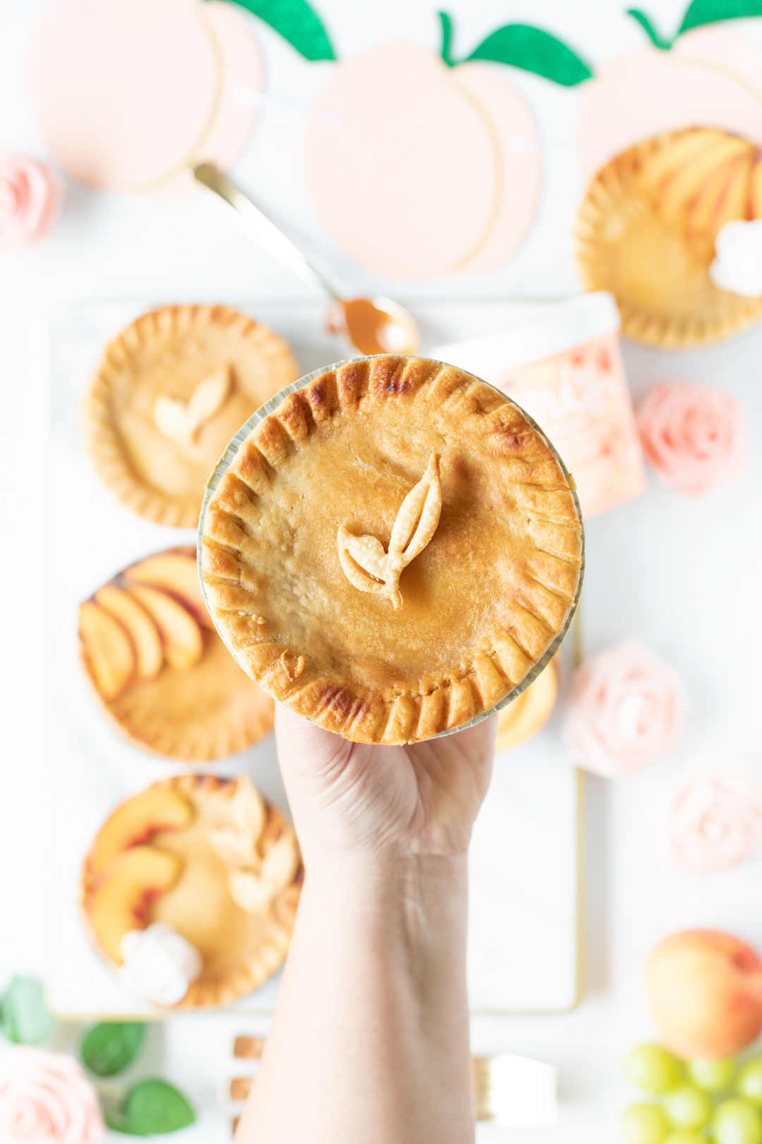 mini peach pie being held by woman's hand. Pretty leaf made out of pie crust on top.