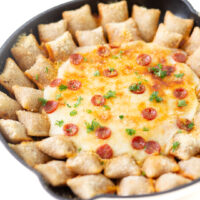 cheesy pepperoni dip up close being served in a skillet with totinos pizza rolls, melted cheese, crispy mini pepperoni and snipped parsley garnish.